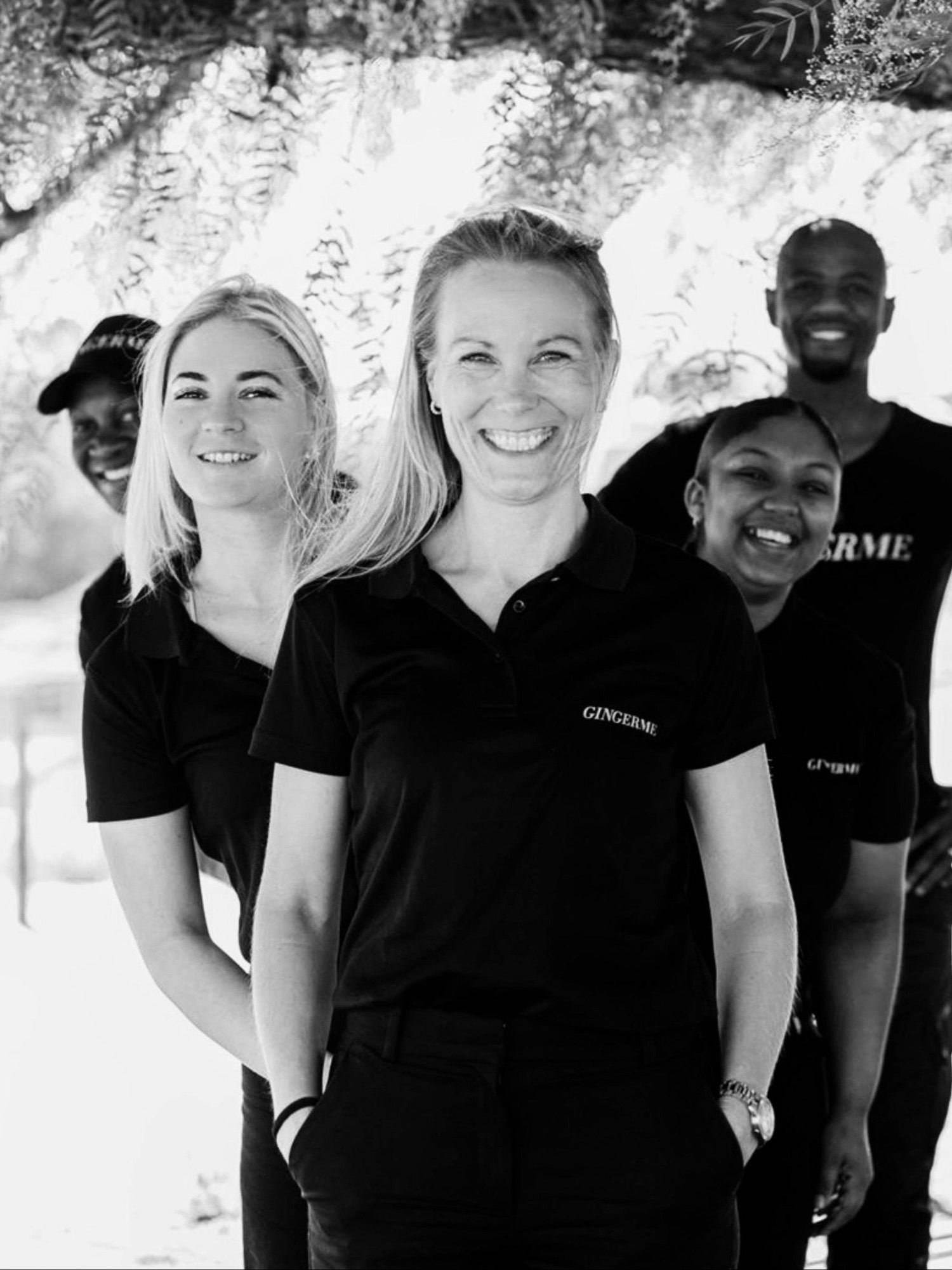 Group of people standing together outdoors, wearing black shirts with 'GingerMe' logo on.