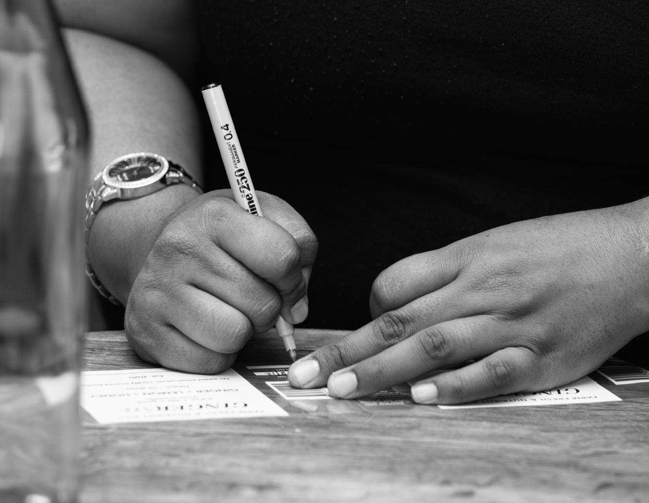 Person holding a pen and signing a document with another hand on a table.
